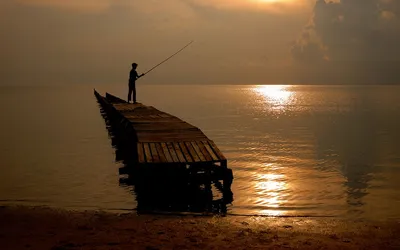 Обои на рабочий стол Мальчик, держащий в руках удочку, стоящий на  деревянных мостках, уходящих в глубь моря, ловит рыбу на фоне утреннего  золотистого солнца, отражающегося на водной поверхности, фотография Игоря  Щербины, обои