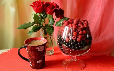Обои на рабочий стол В стеклянном фужере насыпаны ягоды малины, красной и  черной смородины, рядом стоит кружка с налитым кофе, небольшая стеклянная  ваза с водой и красными розами, обои для рабочего стола,