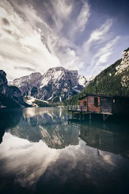 Фото Красивый пейзаж, деревянный дом стоит на берегу горного озера, в  небесах плывут облака