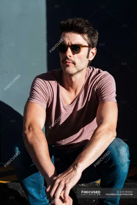 Средний взрослый мужчина в солнечных очках, сидящий у стены в солнечный  день — на открытом воздухе, 30 40 лет - Stock Photo | #476783556