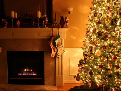 Обои на рабочий стол Уютный новогодний интерьер - наряженная ёлка стоит  возле камина, на котором висят носки для подарков, обои для рабочего стола,  скачать обои, обои бесплатно
