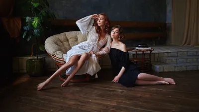 Обои на рабочий стол Модель Аня в черном платье сидит на полу комнаты и  держит под руку модель Олю в белом платье, сидящую на кресле, фотограф  Сергей Жирнов, обои для рабочего стола,